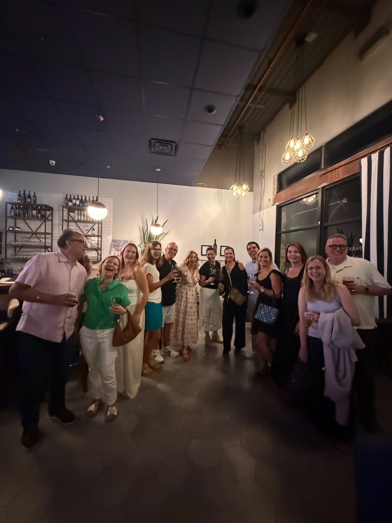 A big group of smiling Steiner Ranch neighbors holding drinks at the Community Nightcap after the first Dinner Club.